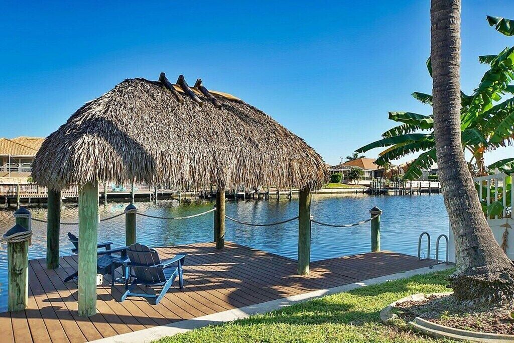 Una estructura con techo de paja, con asientos, una terraza de madera y una masa de agua al fondo.