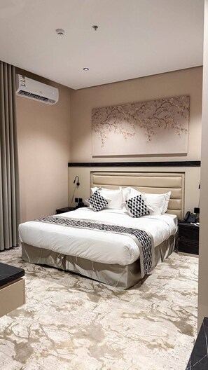 Quarto de hotel com uma cama grande, uma mesa de cabeceira, ar condicionado fixado na parede e um objeto decorativo sobre a cama.