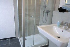A modern bathroom with a glass shower enclosure, a white sink, and a mirror above the sink. - Beach Villa Kleckerburg (Langeoog)