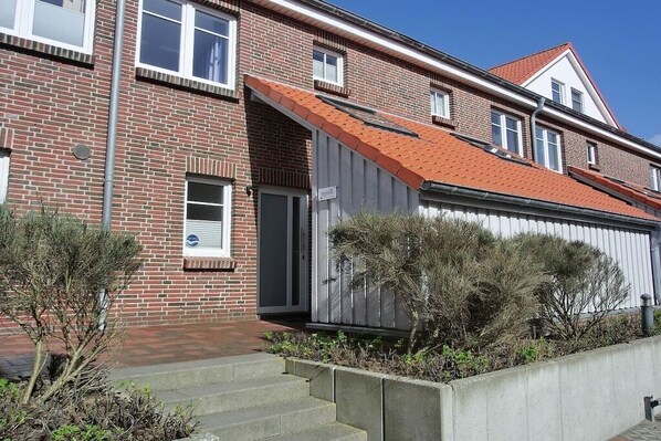 A two-story brick building with a red-tiled roof, a small attached garage, and a concrete staircase leading to the entrance. - Beach Villa Kleckerburg (Langeoog)