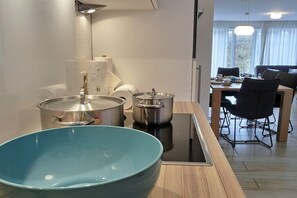 A modern kitchen with a blue bowl, stainless steel pots, and a dining area with a table and chairs. - Beach Villa Kleckerburg (Langeoog)