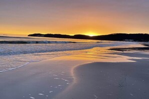 Ranta, jossa näkyy auringonlasku, aallot ja kaukainen maa-alue.