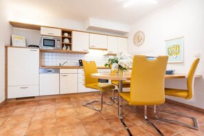 Une cuisine moderne avec des meubles blancs, un four à micro-ondes et un coin repas agrémenté de chaises jaunes et d’une table ronde.