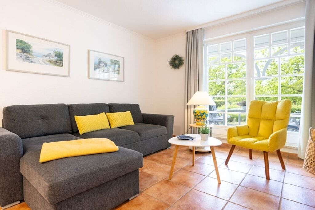 A living room with a grey sofa, a yellow armchair, a small white table, and two framed pictures on the wall.