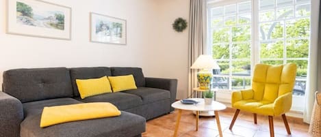 A living room with a grey sofa, a yellow armchair, a small white table, and two framed pictures on the wall.