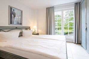 Hotellihuone, jossa on suuri sänky, yöpöytä lampun kanssa, ikkuna verhoilla ja taulu seinällä.