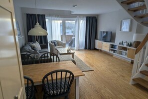 A modern living room with a sofa, a dining table, and a TV. - Apartment in Laboe with swimming pool (Laboe)