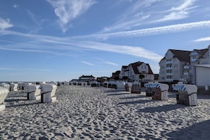 A beach with rows of beach chairs and umbrellas, a row of houses in the background, and a clear sky. - Apartment in Laboe with swimming pool (Laboe)