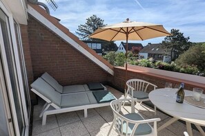 A balcony with a lounge area, a table with chairs, and an umbrella. - Apartment in Laboe with swimming pool (Laboe)