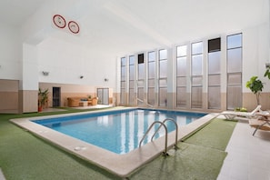 An indoor swimming pool with a clear view of the pool area, a lounge area with seating, and a large windowed wall. - Cozy Studio Apartment in Cala Del Pino with Wi-Fi and Air Conditioning (Cartagena)