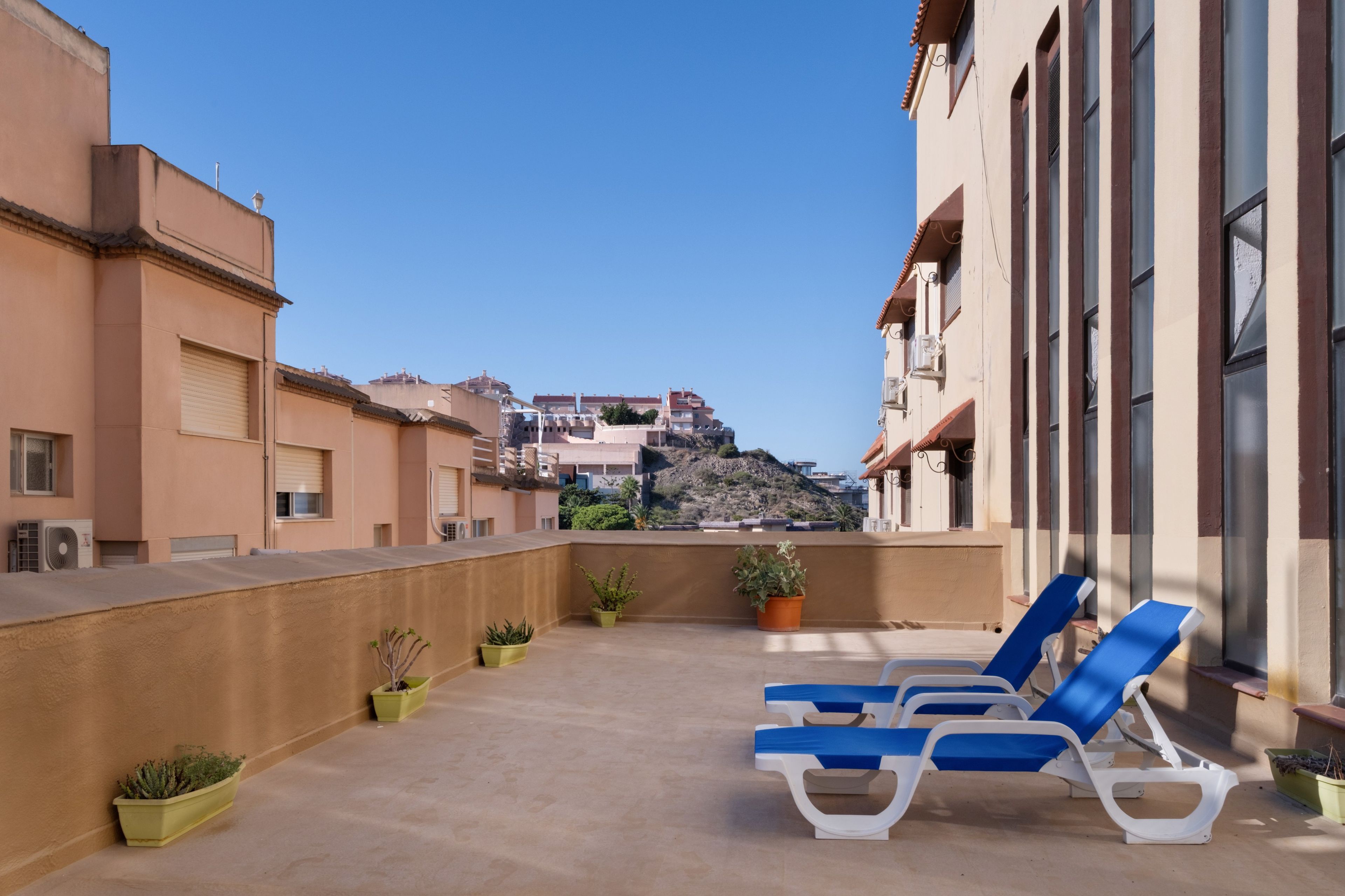 A rooftop terrace with lounge chairs and potted plants, overlooking a cityscape.