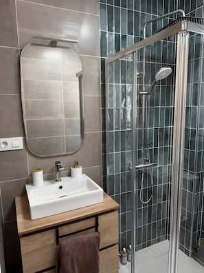 Ein modernes Badezimmer mit einer in Glas eingefassten Dusche, einem weißen Waschbecken und einem Holzbadezimmermöbel.