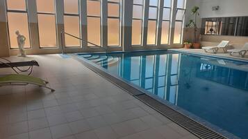 Ein überdachter Pool mit Panoramafenstern, Fliesenboden und Liegestühlen am Pool.