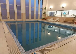 Une piscine intérieure avec un bord carrelé, des chaises longues et une plante en pot.