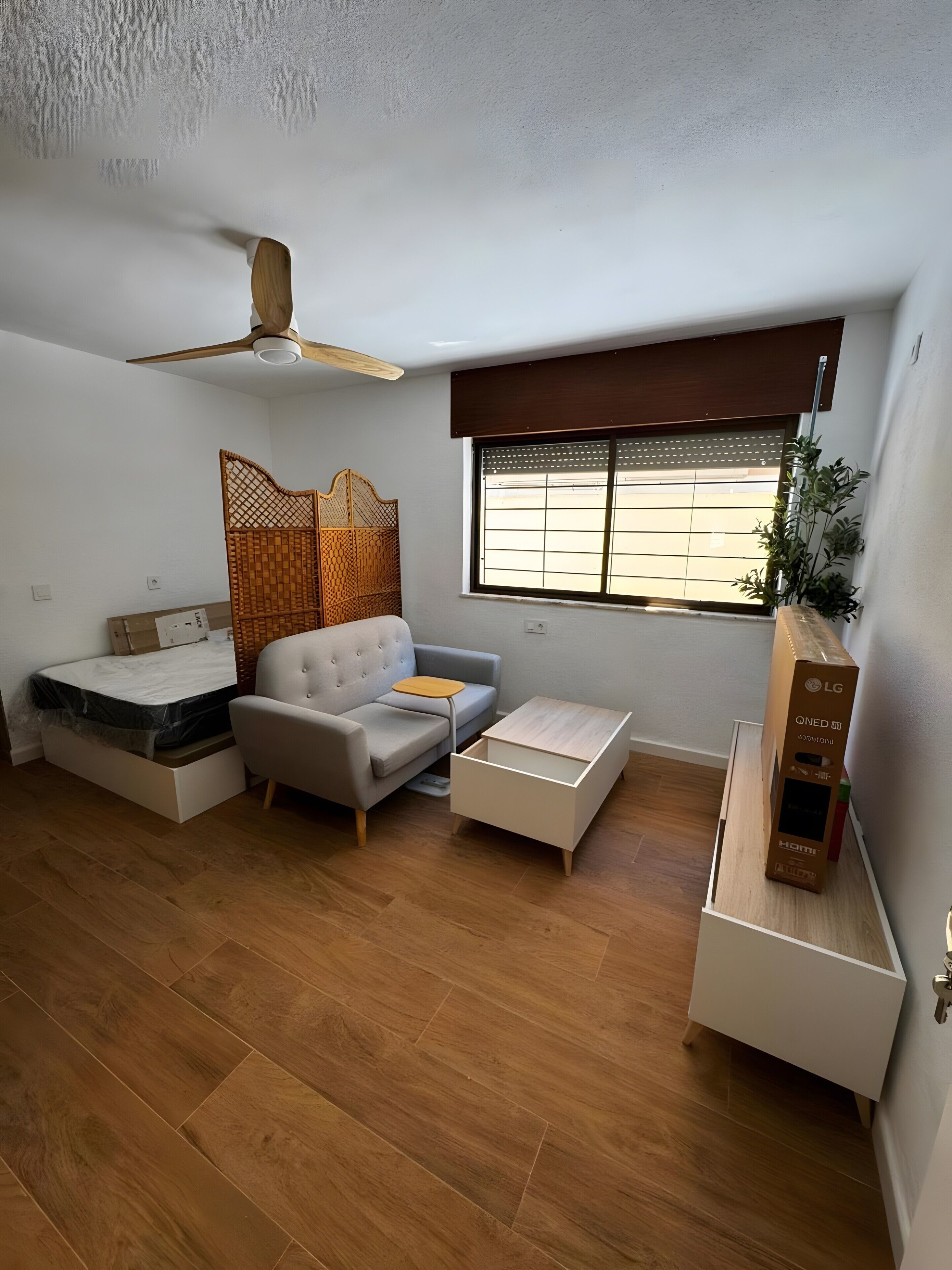 Ein gemütlicher Wohnraum mit Sofa, kleinem Tisch, Bett mit Stauraum, Deckenventilator und Fenster mit Aussicht.