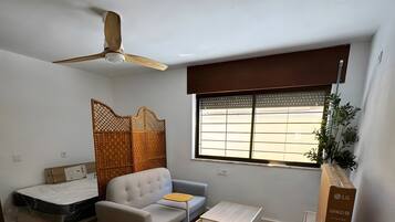 Ein gemütlicher Wohnraum mit Sofa, kleinem Tisch, Bett mit Stauraum, Deckenventilator und Fenster mit Aussicht.