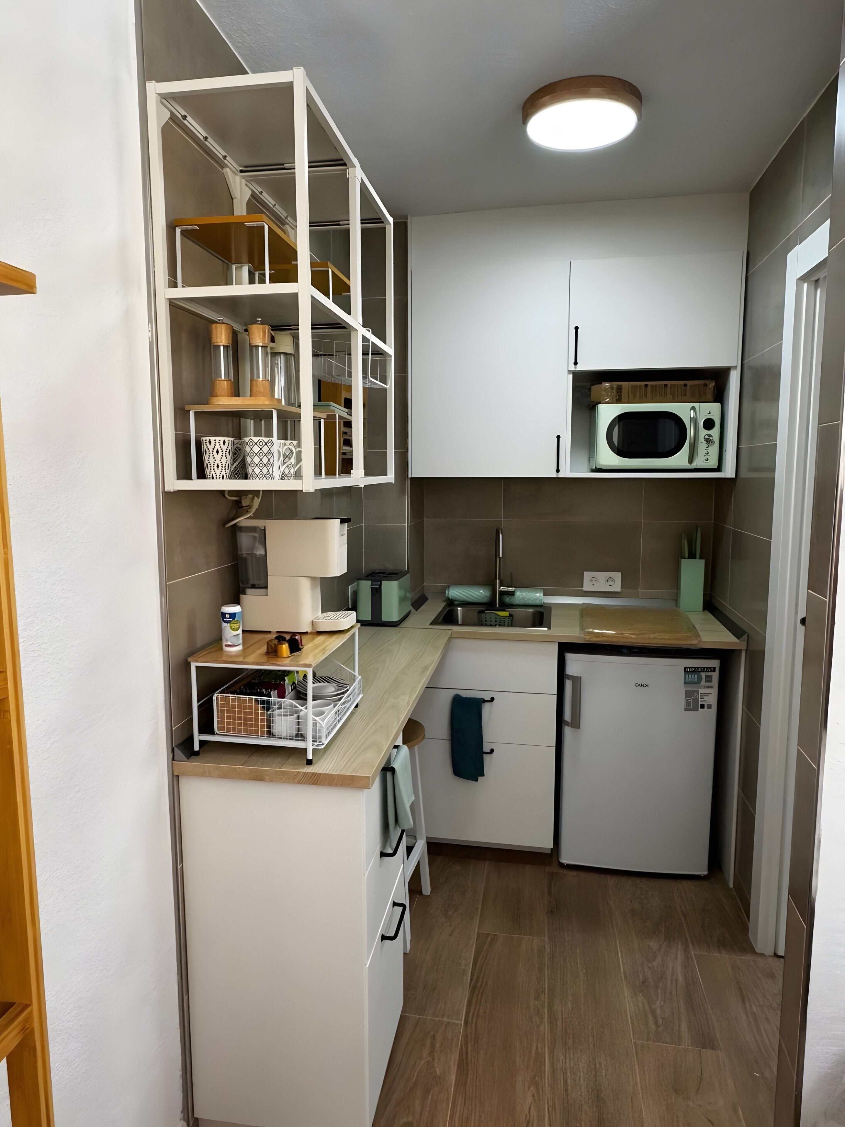 A compact kitchen with white cabinets, a microwave, a toaster, and a small refrigerator.