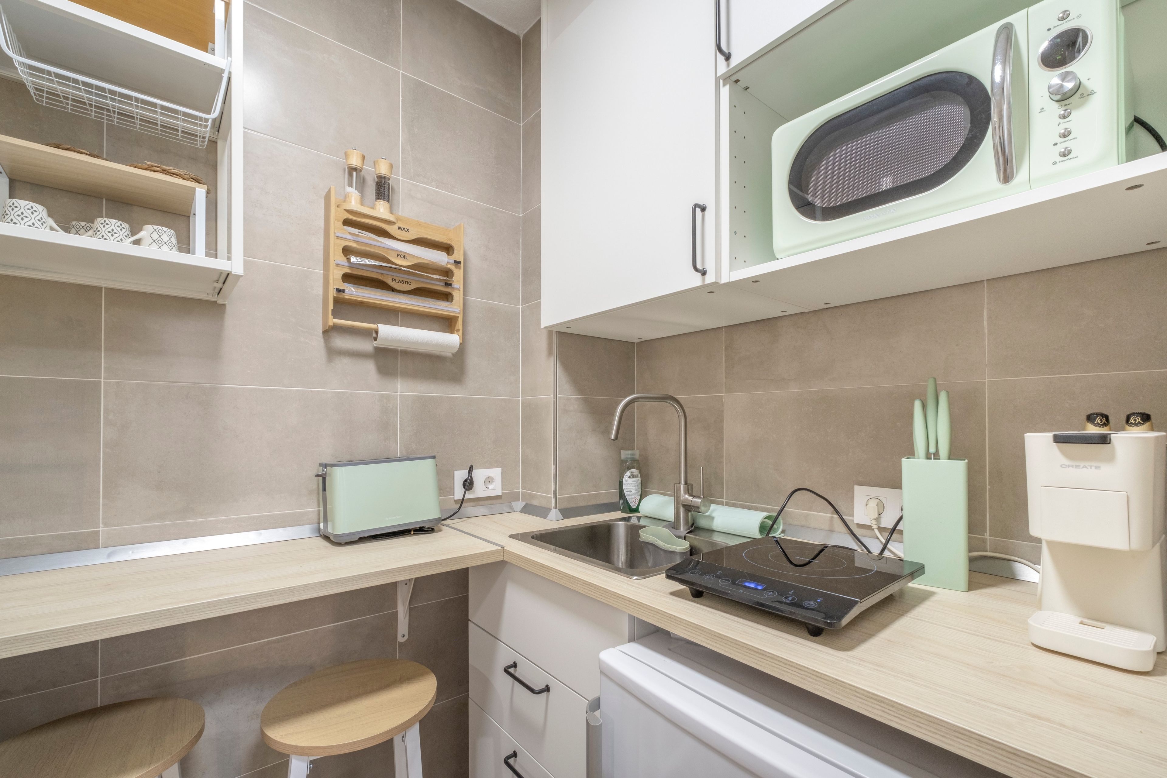 A modern kitchen with a microwave, a kettle, and a kettle holder on the countertop.