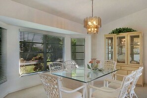 A dining area with a glass table surrounded by white chairs, a hanging light fixture, and a cabinet with glass doors. - CCVS - Bimini Sunset (Cape Coral)