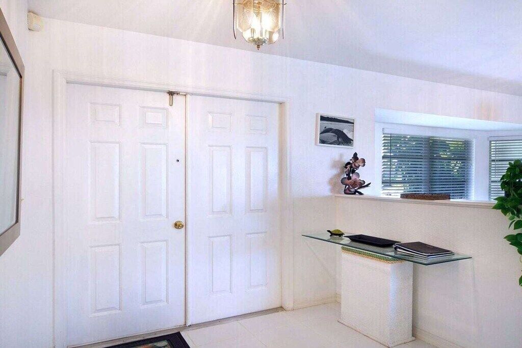 A hallway with a double door, a glass table with books, a wall-mounted picture, and a window with blinds.