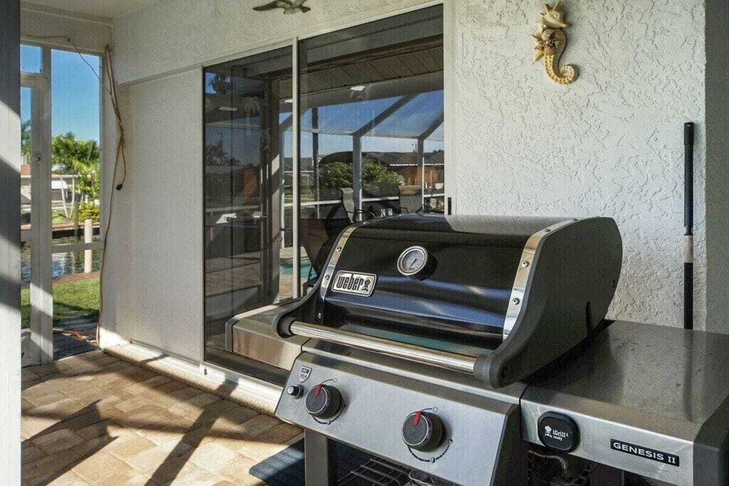 An outdoor grill area with a Weber Genesis II grill, a glass door leading to a patio, and a decorative wall ornament.