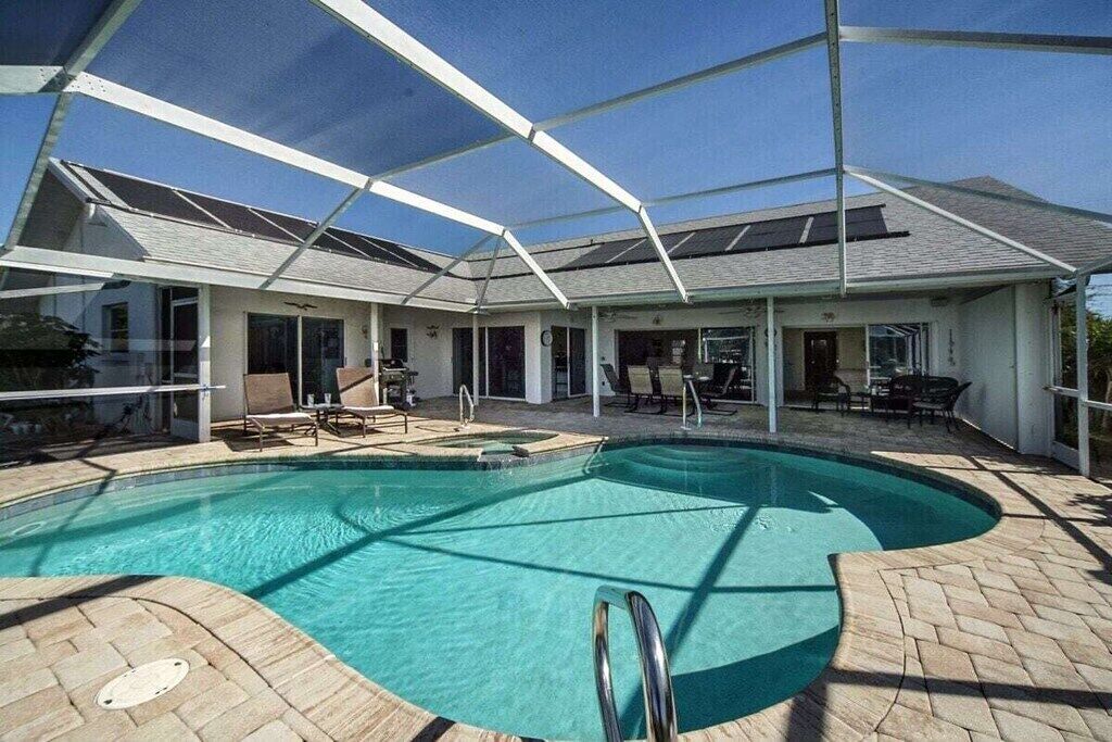 Ein Schwimmbecken mit überdachter Terrasse, Sonnenschutz und blauem Himmel.