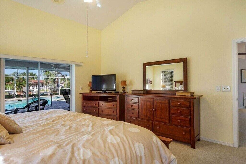 Une chambre à coucher comprenant un lit, une télévision, une commode et une grande fenêtre donnant sur un espace piscine.