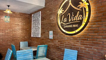A restaurant interior with a brick wall, a sign reading 'La Vida Chiang Mai', and blue chairs around a table.