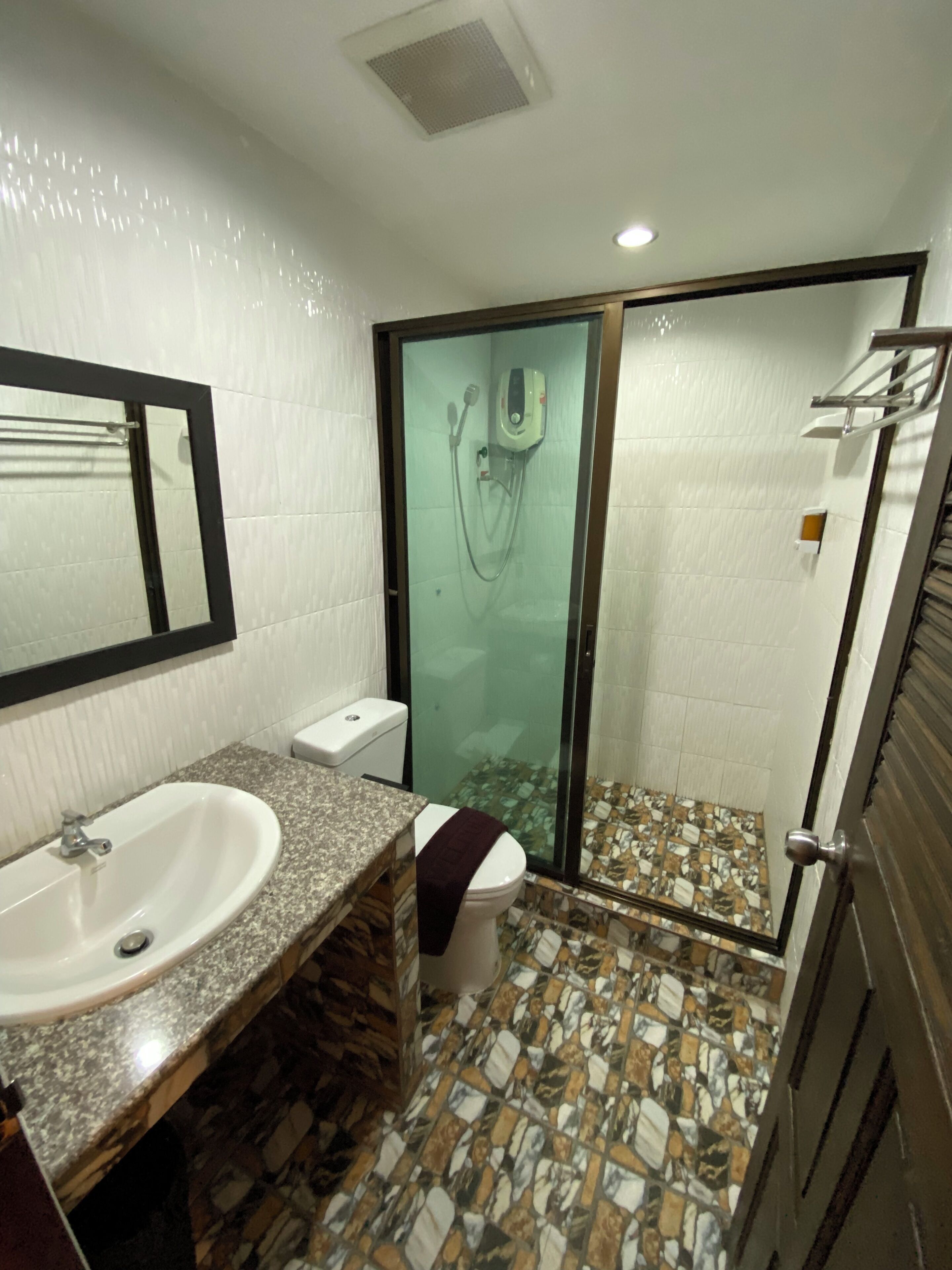 Un baño con lavamanos de encimera de granito, inodoro, cabina de ducha con mampara de vidrio y suelo de baldosas.