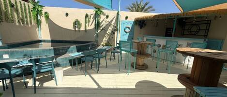 An outdoor patio with tables and chairs, a pool, and a bar area.