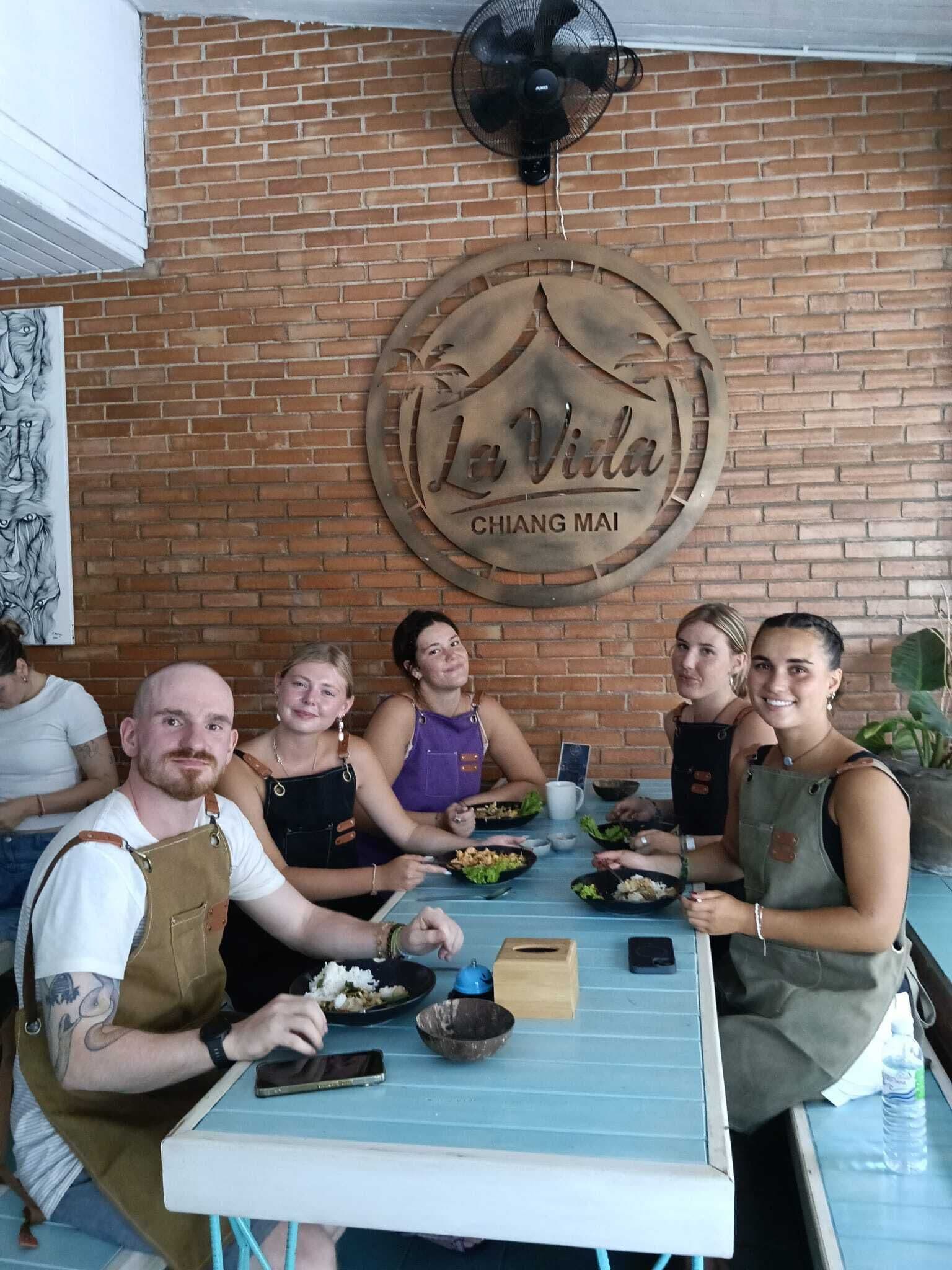 Un grupo de personas cenando en un restaurante con una pared de ladrillo y un letrero circular sobre la mesa.