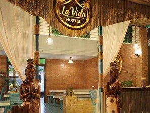 A hostel interior with a central sign reading 'La Vida HOSTEL,' two statues, brick walls, and hanging lights. - La Vida Hostel Chiang Mai (Mueang Chiang Mai)