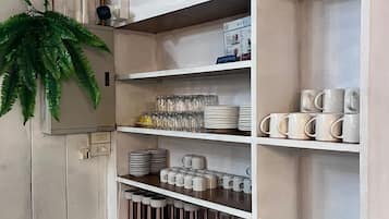Un mueble blanco con varios estantes que contiene tazas, platos y vasos.