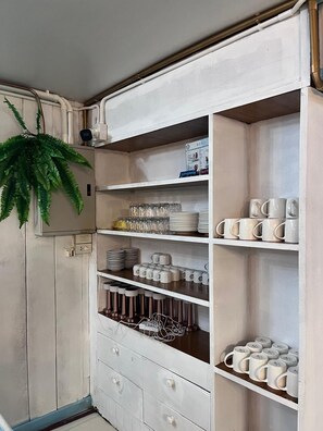 Un mueble blanco con varios estantes que contiene tazas, platos y vasos.