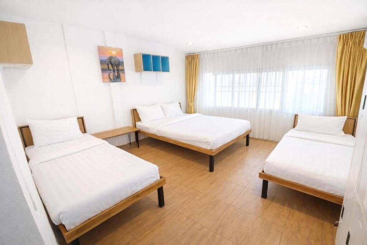 Ett hotellrum med tre separata sängar, ett stort fönster med gardiner och ett konstverk som hänger på väggen.