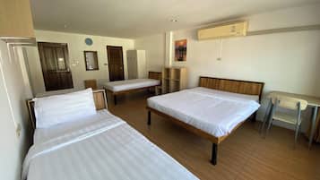 A hotel room with three single beds, a desk, a chair, a wardrobe, and a clock on the wall.