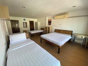 Ett hotellrum med tre enkelsängar, ett skrivbord, en stol, en garderob och en väckarklocka på väggen.