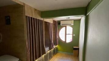 Un estrecho pasillo con una cama a la izquierda, una ventana con cortinas y una puerta al final.