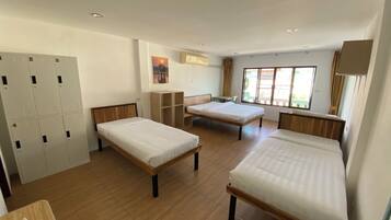 Un dormitorio con tres camas individuales, un armario, un escritorio y una ventana con cortinas.