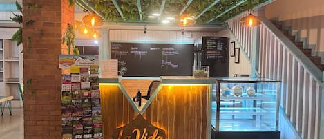 A coffee shop named 'La Vida' with a wooden counter, a menu board, and a staircase to the right.