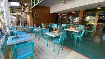 An outdoor seating area with tables and chairs, a ceiling fan, and potted plants.
