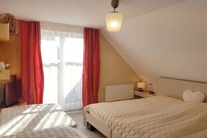 Een slaapkamer met een bed, een nachtkastje met een lamp, een raam met gordijnen en een radiator.