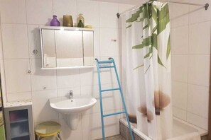 Een badkamer met een witte wastafel, een spiegel erboven, een blauwe ladder en een douchegordijn met bladmotief.