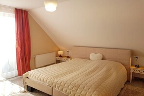 A bedroom with a bed, a nightstand, a lamp, a radiator, and a window with curtains. - Holiday apartment with 2 bedrooms (Koserow)