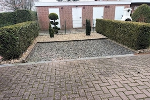 A paved courtyard with a brick pathway, trimmed hedges, and a small tree. - Pennekamp Carolinensiel (Carolinensiel)