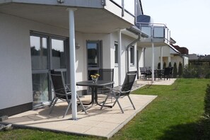 Un edificio moderno con un patio cubierto que incluye una mesa, sillas, un pequeño jardín y vistas del vecindario.