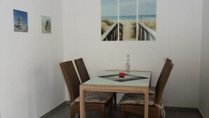 Uma área de refeições com mesa e quatro cadeiras, uma garrafa de licor, e uma parede com três quadros.