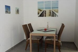 Un comedor con una mesa, cuatro sillas, una botella de licor y una pared adornada con tres cuadros enmarcados.