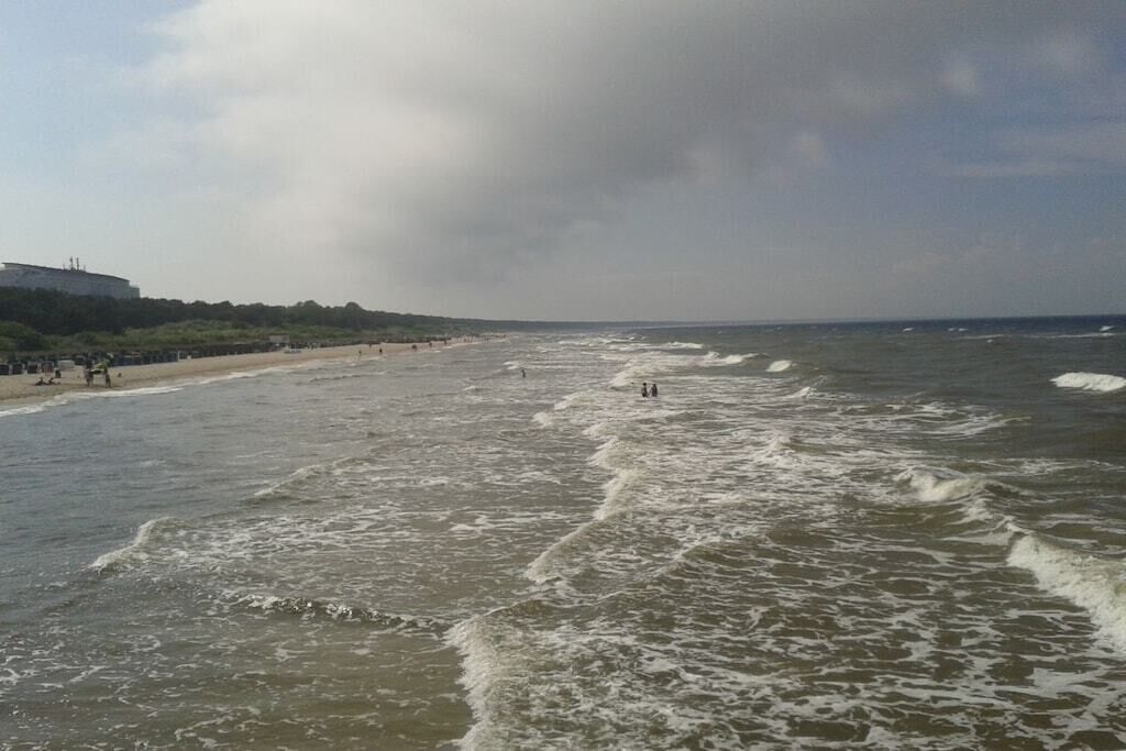 A beach with waves, a few people, and a building in the distance.