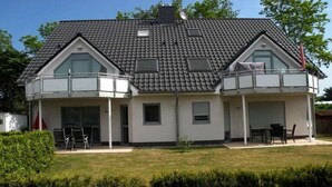 Uma casa de dois andares com varanda no andar superior, pequeno alpendre e céu claro.